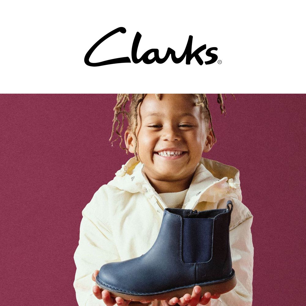 child holding a boot and smiling with the clarks logo at the top