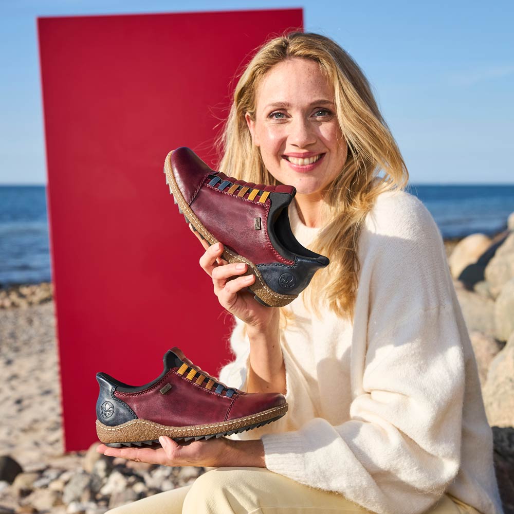 woman holding a pair of rieker shoes sat by the beach
